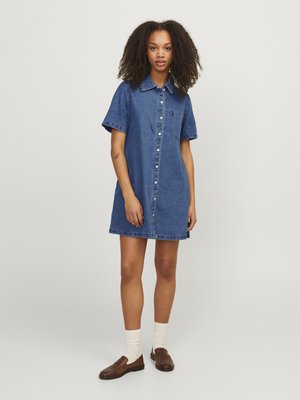 Abito camicia in denim, maniche corte, azzurro chiaro, con bottoni all'anteriore, tasca applicata, lunghezza al ginocchio, abbinato a scarpe marroni e calzini crema.