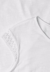 Tissu blanc en gros plan montrant un décolleté en V et une manche avec un délicat bord en dentelle blanche sur un tissu en coton doux.