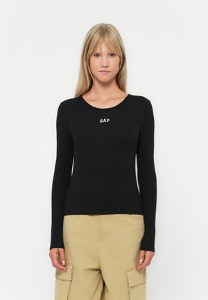 Black ribbed long-sleeve top with a round neckline and white "GAP" logo on the chest, paired with beige cargo pants.