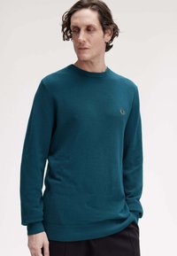 Maglione a maglia color turchese con scollatura a girocollo, polsini e orlo a costine, caratterizzato da un piccolo logo ricamato sul petto. Texture liscia e maniche lunghe.