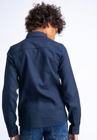 Camicia blu navy con maniche lunghe e colletto a punta, dotata di dettaglio yoke sulla parte posteriore e accenti di bottoni a contrasto.