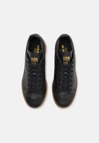 Svarta lädersneakers med perforerade sidodetaljer, en gummisulor och guldbranding på tungan. Snörningsdesign med platta snören.