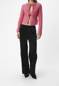 Cardigan court en tricot rose avec deux liens au niveau de l'encolure, associé à un pantalon en velours côtelé noir taille haute. Texture lisse et coupe décontractée.