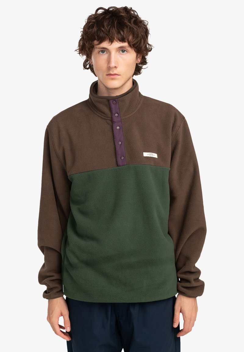 Sudadera de forro polar con parte superior marrón y parte inferior verde, cuello alto, tapeta de botones morada y pequeño logotipo en el pecho.