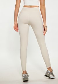 Beige leggings met een hoge tailleband, slim fit en een gladde textuur, gecombineerd met grijze en witte sport sneakers.