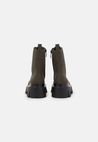 Bottines en simili cuir vert avec une semelle épaisse noire, fermeture éclair et détails de couture contrastés. Texture lisse et design élégant.