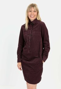 Burgundy kordfløjl skjortekjole med knap-ned krave, enkelt brystlomme og lange ærmer. Har sidelommer og struktureret stof.