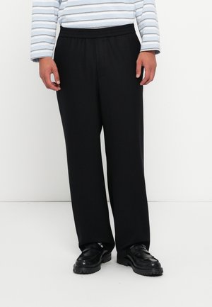 Black, loose-fitting trousers with an elastic waistband, made from a smooth fabric. Paired with black shoes and a striped long-sleeve shirt.