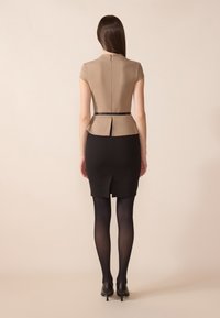 Béžový peplum top se zipem na zadní straně, v kombinaci s černou upnutou sukní s rozparkem vzadu. Vzhled doplňují štíhlé černé punčocháče a vysoké podpatky.