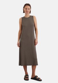 Ärmelloses Kleid in einem schwarz-beigen geometrischen Muster. Knielange Länge, aus weichem Stoff gefertigt. Kombiniert mit dunklen Sandalen für einen Kontrast.