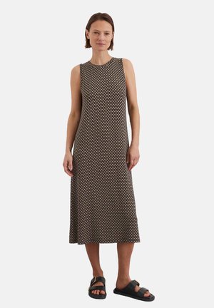 Ärmelloses Kleid in einem schwarz-beigen geometrischen Muster. Knielange Länge, aus weichem Stoff gefertigt. Kombiniert mit dunklen Sandalen für einen Kontrast.