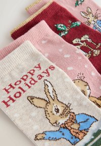 Three pairs of patterned socks: cream with a rabbit graphic and "Hoppy Holidays," pink with white dots, and dark red with holiday motifs.
