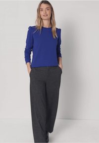 Königsblaues Langarm-Top mit Schulterakzenten, kombiniert mit locker sitzenden dunkelgrauen Hosen. Glatte Stoffstruktur, entspannte Passform.