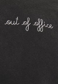 Camicia di cotone nera con ricamo bianco che recita "out of office" in un font corsivo, realizzata in un tessuto morbido e testurizzato.