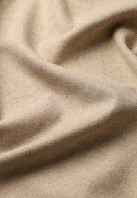 Beige uldstof med en blød, glat tekstur, der har en let glans og subtile nuancer i farven, draperet i bløde folder.