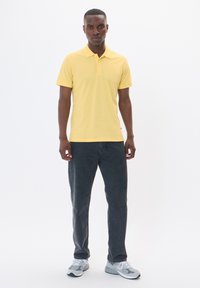 Gul pikétröja med krage, kort ärm; kombinerad med mörkgrå jeans och grå sneakers. Enkel design, slät textur, utan mönster.