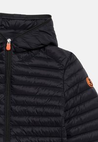 Μαύρο καπιτονέ μπουφάν με κουκούλα, μπροστινό φερμουάρ με πορτοκαλί τριχιά και πορτοκαλί κυκλική λογότυπη μπαλώμα στον άνω μανίκι.