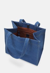Sac cabas en denim bleu avec double poignée, ouverture au sommet, doublure intérieure marron et poche intérieure zippée avec détail boucle.