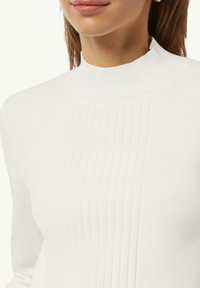 White ribbed turtleneck sweater featuring a fitted design, smooth texture, and subtle vertical lines; ideal for layering and warmth.