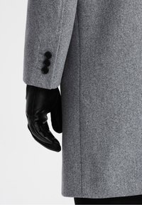 Šedý vlněný kabát s texturovanou látkou, s černou koženou rukavicí na pravé ruce a třemi černými knoflíky na rukávu.