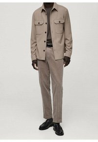 Een tan knoopshirt met twee borstzakken, gecombineerd met lichtbruine corduroy broek en zwarte leren schoenen. Zachte textuur en gestroomlijnd ontwerp.