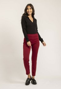 Haut noir à manches longues côtelé avec un col, associé à un pantalon bordeaux taille haute et coupe slim, et des mocassins noirs sur un fond neutre.