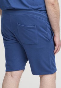 Blå bomuldsshorts med elastisk taljebånd, med en enkelt baglomme og glat tekstur, vist fra en sidevinkel.