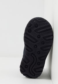 Suola di scarpa in gomma nera con un motivo testurizzato, incluse scanalature e battistrada circolari, che evidenziano caratteristiche di durata e aderenza.