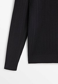 Manche de pull noir en maille et bas latéral montrant un motif en chevrons texturé avec poignet et ourlet côtelés sur fond blanc.