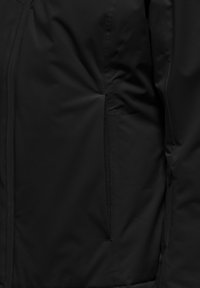 Černá, lehká bunda s hladkým povrchem, zipovými kapsami a minimalistickým designem. Tkanina vypadá jako voděodolná.