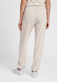 Beige sweatpants with an elastic waistband and tapered cuffs, made of soft, textured fabric. Paired with white sneakers.
