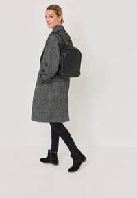 Szary, teksturowany wełniany płaszcz na czarnych dżinsach; czarna skórzana plecak i czarne zamszowe botki za kostkę z niskim obcasem. Prosty, funkcjonalny design.