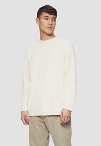 Langärmliges Cremeshirt mit Rundhalsausschnitt, aus weichem Stoff, mit lässigem Schnitt und subtiler Textur, kombiniert mit hellbeigen Hosen.