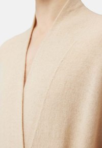 Beige kashmircardigan med V-ringning. Har en mjuk textur och subtila sömnadsdetaljer längs halsringningen, visad från en närbild.