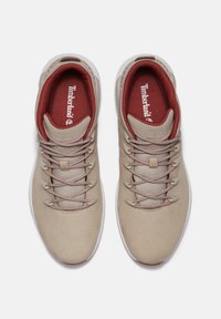 Beige Sneaker mit Obermaterial aus Mesh und Leder, runder Zehenform und Gummisohle. Verfügt über ein rotes Innenfutter und kontrastierende Schnürsenkel. Timberland-Branding sichtbar.