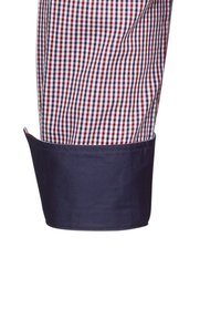 Tessuto della camicia a quadri in rosso, bianco e blu, con un polsino blu navy dalla trama liscia. Il polsino è ripiegato, mostrando i dettagli delle cuciture.