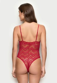 Body rojo de encaje con patrones en zigzag, tirantes ajustables y un diseño de tanga en la parte trasera. La tela parece delicada y transparente.
