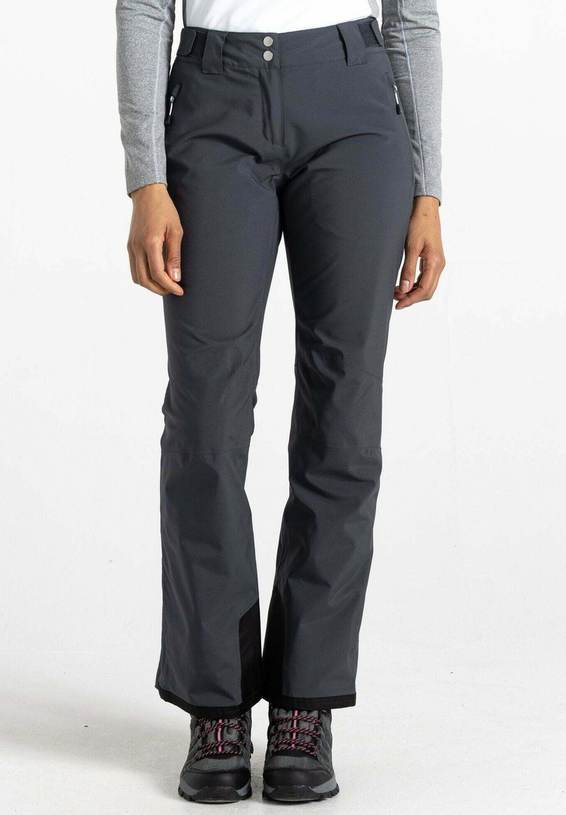 Graue wasserdichte Schneehosen mit einem Bund, der über zwei Knöpfe verfügt, seitlichen Reißverschlusstaschen und Belüftungen an den Knöcheln, kombiniert mit schwarzen Wanderschuhen.