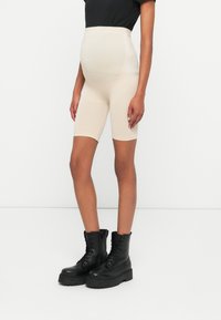 Beige, magas derekú kismama sort, rugalmas anyagból, amely a comb közepéig ér, fekete, fűzős bokacsizmákkal, vastag talppal párosítva.