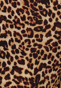 Leopardmönstrad tyg med en beige bakgrund och bruna samt svarta fläckar, som visar en mjuk textur och varierande fläckformer.