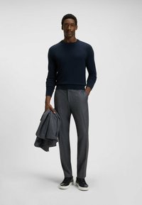 Dark blue sweater, gray textured trousers, black sneakers, holding a gray blazer. Simple and elegant design with fitted silhouette.