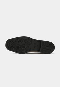 Semelle en caoutchouc avec un motif de traction texturé, présentant un bord lisse. Détails en brun clair avec le logo "GANT" embossé au niveau du talon.