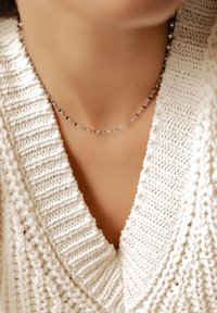 Silberne Kettenhalskette mit abwechselnd glatten und strukturierten Gliedern, getragen über einem cremefarbenen, gestrickten Pullover mit V-Ausschnitt.