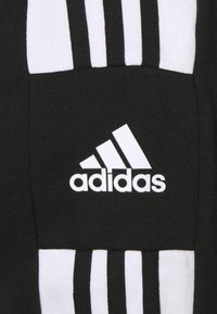 Tissu noir avec des rayures horizontales blanches, arborant un logo Adidas blanc proéminent. Le design est sportif avec une texture douce.