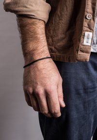 Black elastic bracelet on a hand, featuring a textured, smooth finish. The hand is partially covered by a tan, corduroy shirt sleeve.