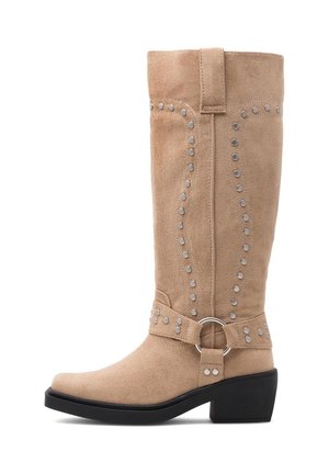 Beżowy zamszowy kozak do połowy łydki z srebrnymi ćwiekami, ozdobnym paskiem i kółkiem wokół kostki oraz niskim czarnym obcasem typu słupek.
