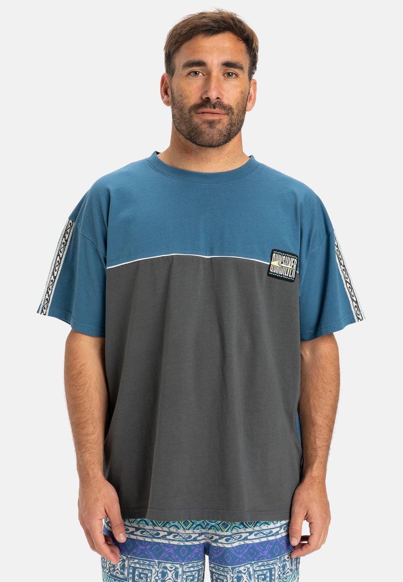 Korte mouwen T-shirt met blauwe en grijze panelen, een ronde hals en een logo patch op de borst. De stof lijkt zacht en heeft een ontspannen pasvorm.