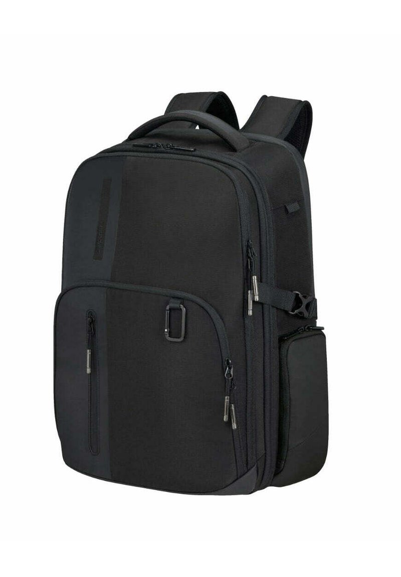 Sac à dos en tissu noir avec plusieurs poches zippées, des bretelles rembourrées et une poche latérale. Présente un design élégant et structuré.