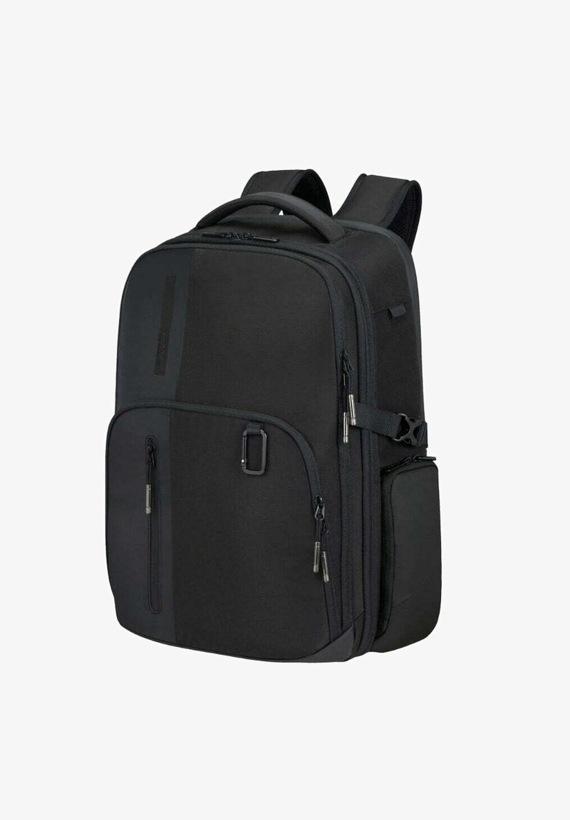 Sac à dos en tissu noir avec plusieurs poches zippées, des bretelles rembourrées et une poche latérale. Présente un design élégant et structuré.