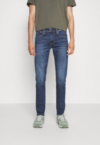Mörkblå denimjeans med slim fit, med en klassisk femficksdesign, kontrasterande sömmar och slitna detaljer vid låren.